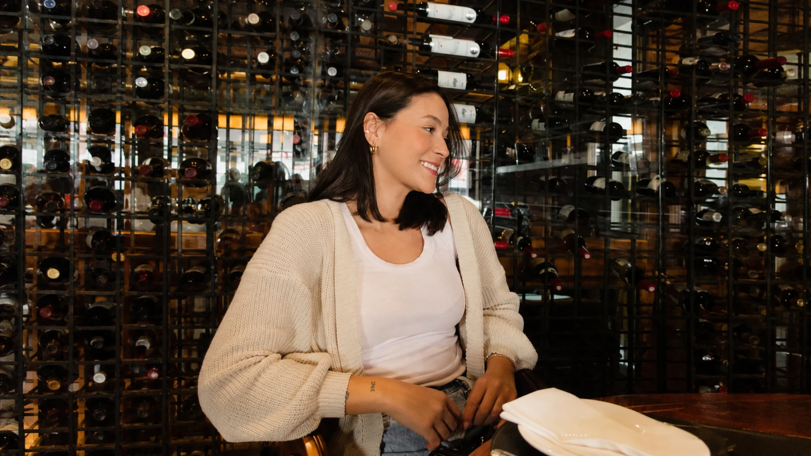 Luiza Soares sorrindo, de cardigã claro, sentada à mesa